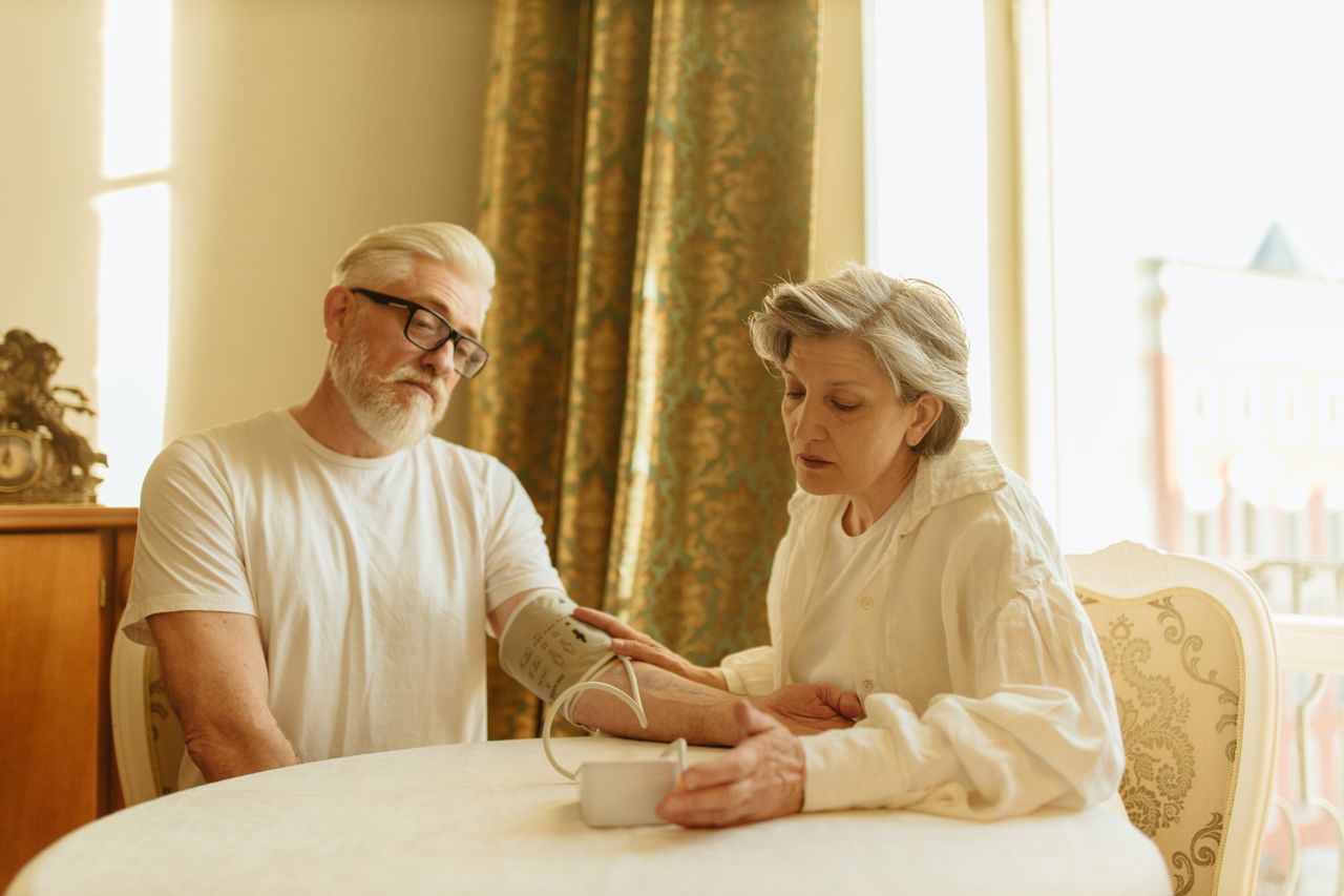 services-01 An elderly couple at home measuring blood pressure with a digital monitor, depicting care and health awareness.